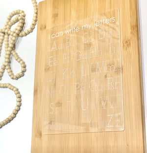 Clear acrylic dry erase tracing board with uppercase and lowercase letters engraved on bamboo background