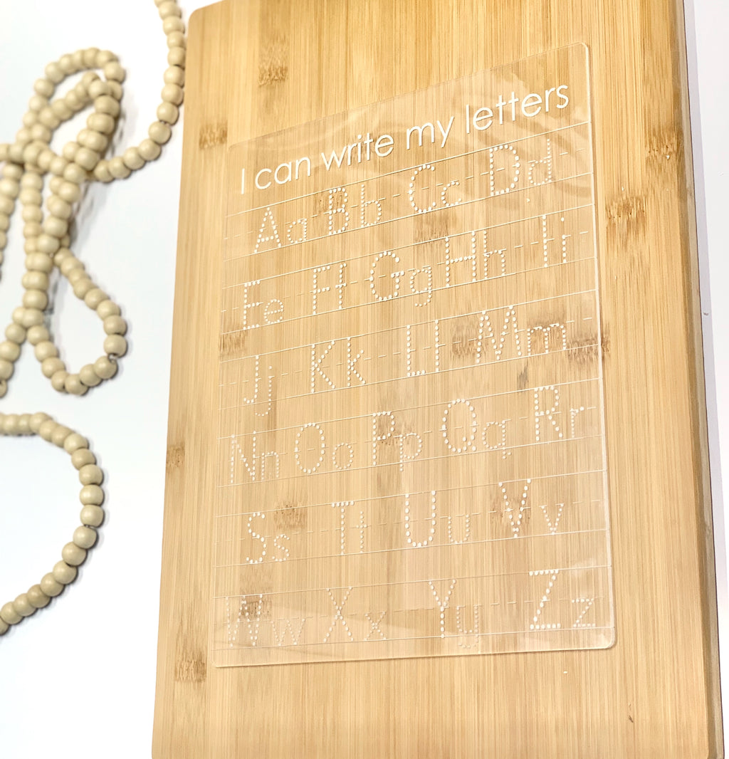 Clear acrylic dry erase tracing board with uppercase and lowercase letters engraved on bamboo background