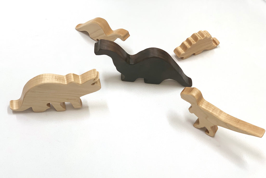 Set of five wooden dinosaur toy figurines in natural and dark wood tones on white background