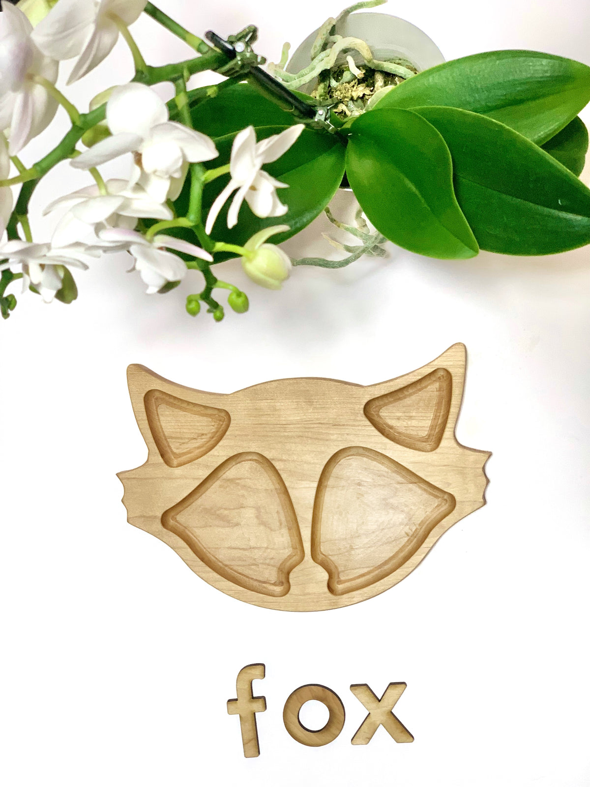 Natural wooden fox-shaped sensory tray with carved compartments and wooden letters spelling fox beneath on white surface