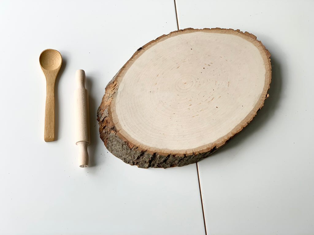 Live edge wooden tray with natural bark edges alongside small wooden spoon and miniature rolling pin on white surface