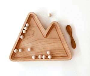 Natural wooden mountain-shaped sensory tray with small wooden beads and a matching wooden spoon on white background
