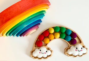 Natural wooden rainbow sensory tray with colorful felt balls and smiling cloud decorations on white surface