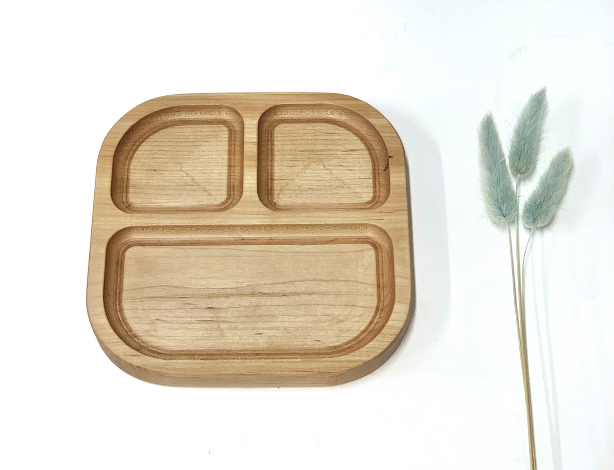 Square wooden sensory tray with three compartments on white background next to dried green floral stems