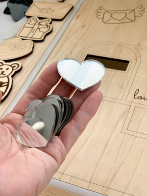 Hand holding set of 7 clear laser-cut heart acrylic shapes for sensory loose parts play on wooden surface