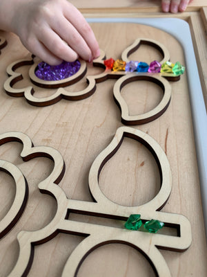 Wooden flower-themed FLISAT table insert with colorful gem beads being placed by a child's hand on light wood surface