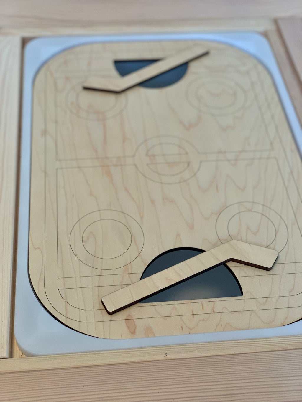 Wooden table top hockey insert with laser-engraved rink design and two small wooden hockey sticks on Flisat bin surface