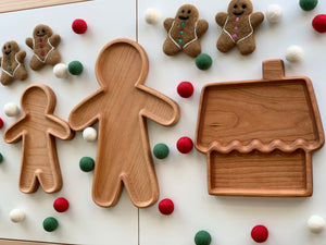 Natural wooden person-shaped large plates and a gingerbread house tray surrounded by felt balls and gingerbread cookies