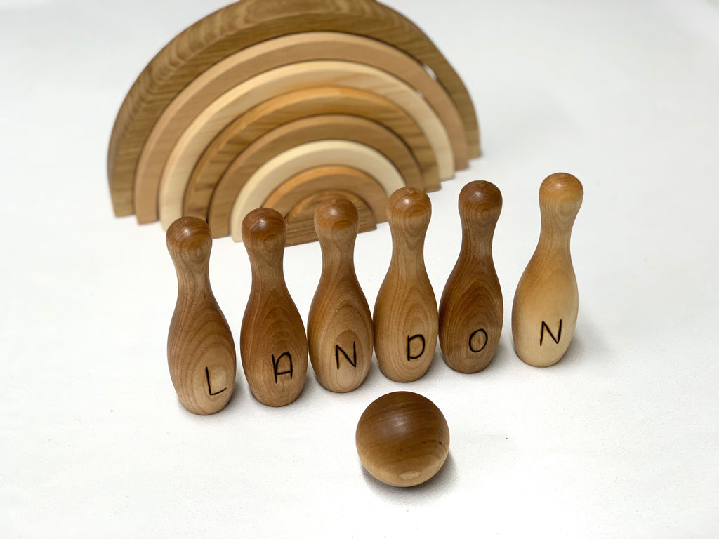 Personalized wooden bowling pins spelling Landon with ball and stacked wooden rainbow toy in background