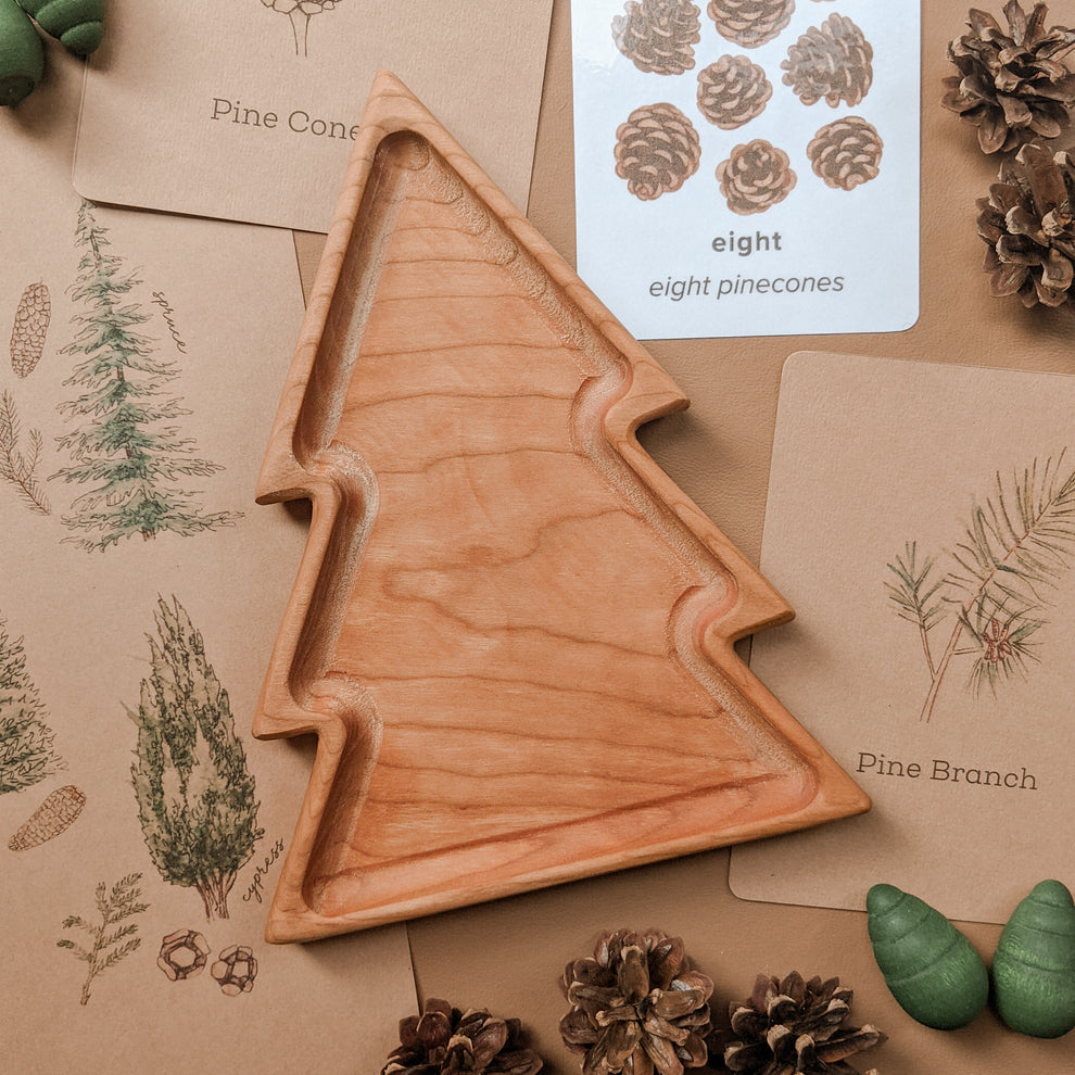 Natural wooden tree-shaped sensory tray with smooth edges on botanical flashcards and pinecone decorations