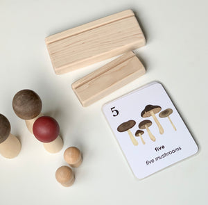 Natural unfinished wooden flash card holders with educational mushroom counting card and wooden peg toys on white background