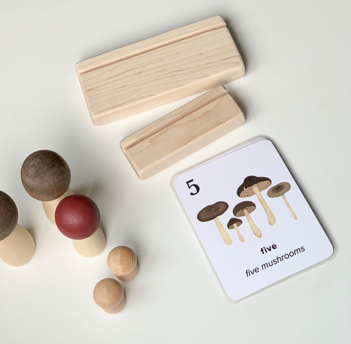 Natural unfinished wooden flash card holders with educational mushroom counting card and wooden peg toys on white background