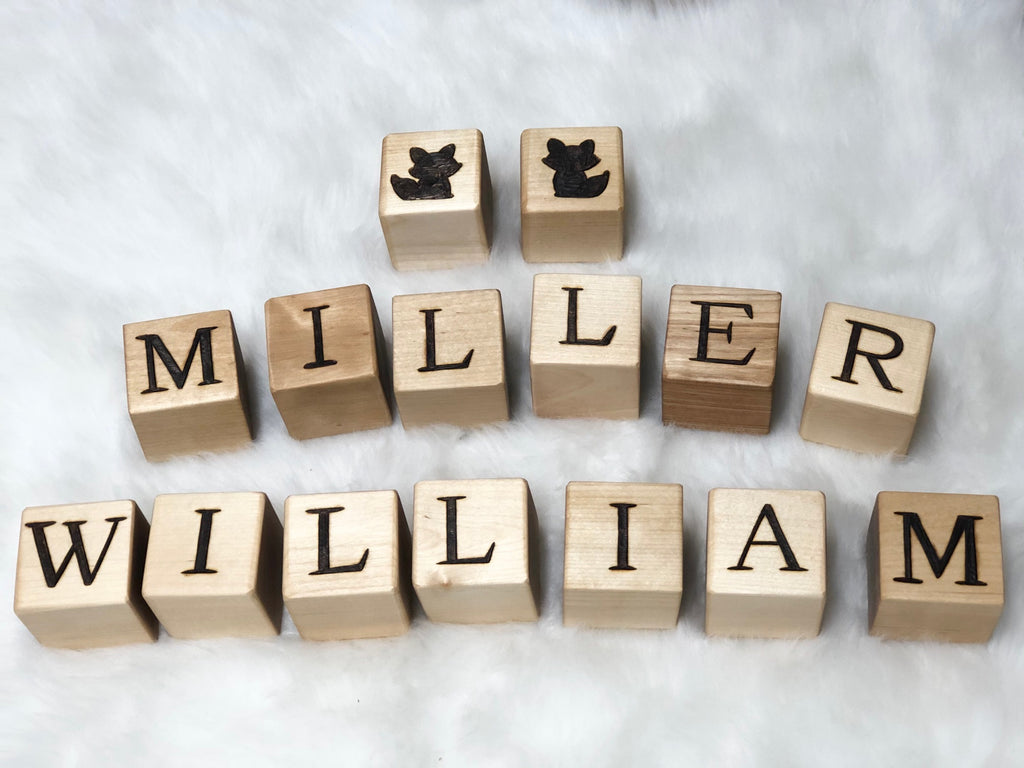 Custom wooden blocks with engraved letters and animal silhouettes arranged on a white surface spelling Miller William