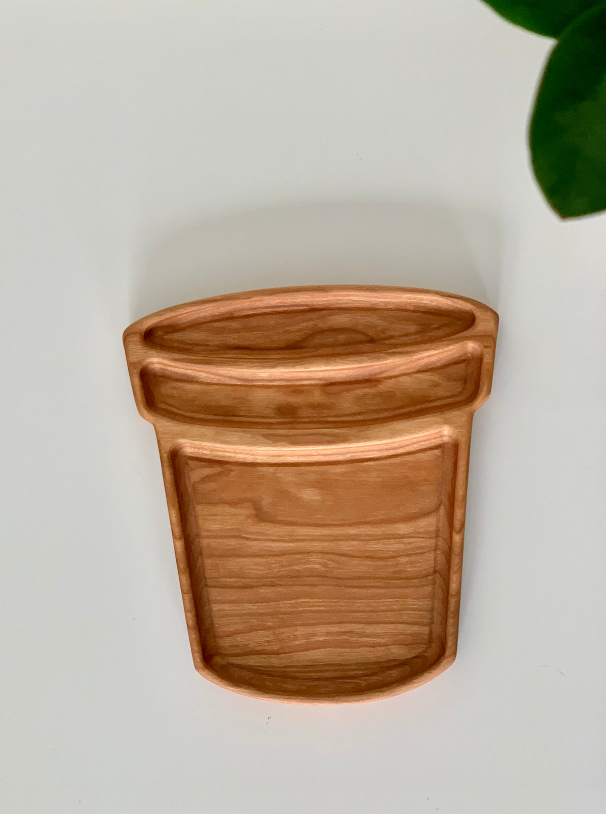 Wooden flower pot shaped sensory tray with three compartments on white surface with green leaf corner visible