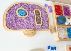Wooden camper-shaped sensory tray filled with colorful sensory materials and small sorting compartments on white surface