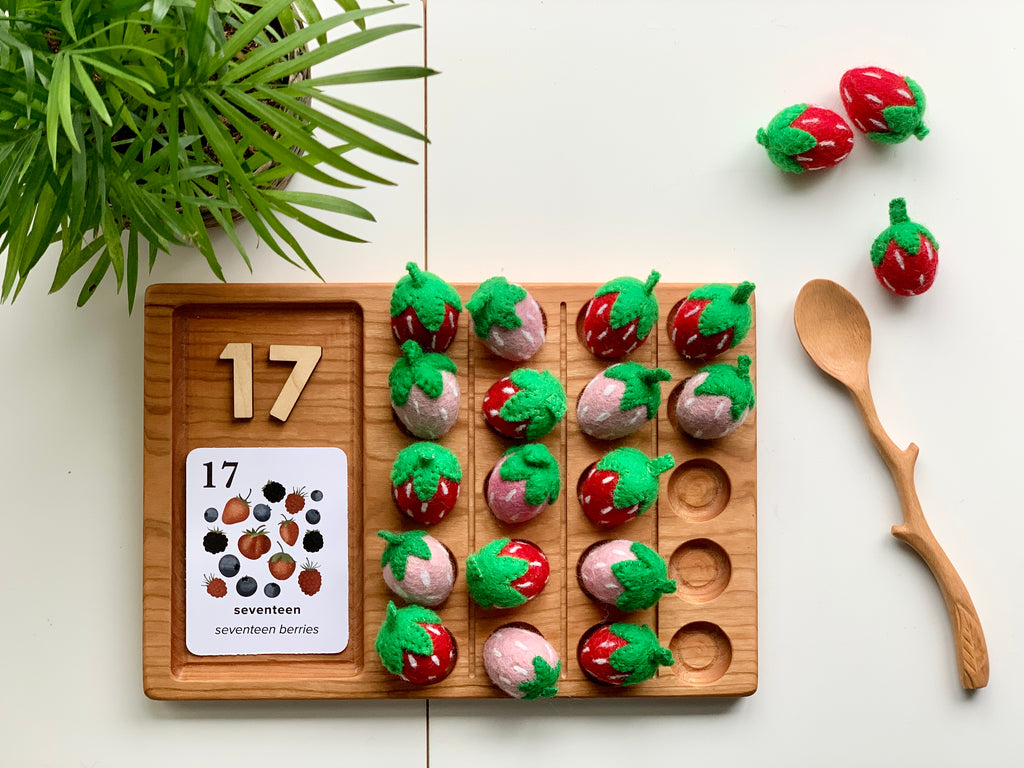 Wooden 20 frame sensory tray with felt strawberries, wooden number tiles showing 17, and carved wooden spoon on white surface