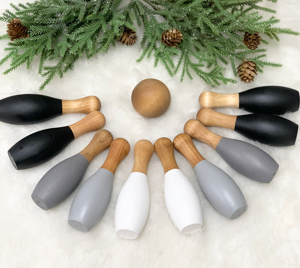 Monochrome wooden 10-piece bowling set with black, gray, and white pins arranged around a wooden ball on white surface with pine branches