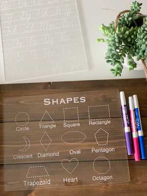 Clear acrylic dry erase board with engraved basic shapes and names for tracing and writing practice with markers nearby
