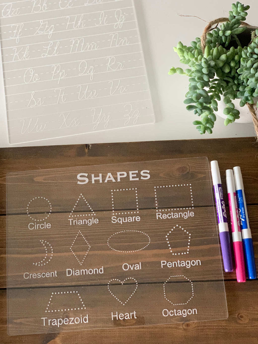Clear acrylic dry erase board with engraved basic shapes and names for tracing and writing practice with markers nearby