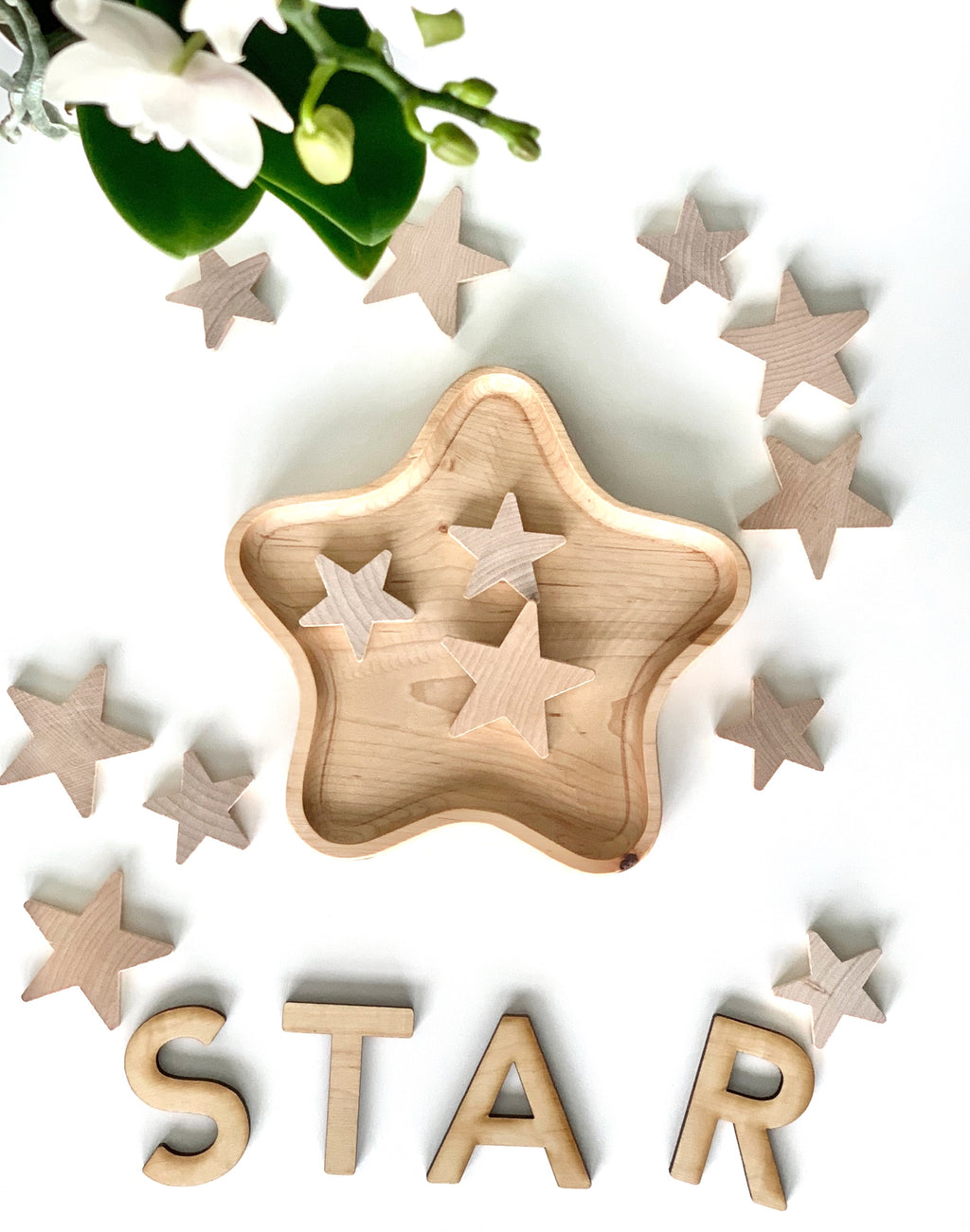Natural wooden star-shaped sensory tray with matching star pieces scattered on white surface near wooden letters spelling STAR