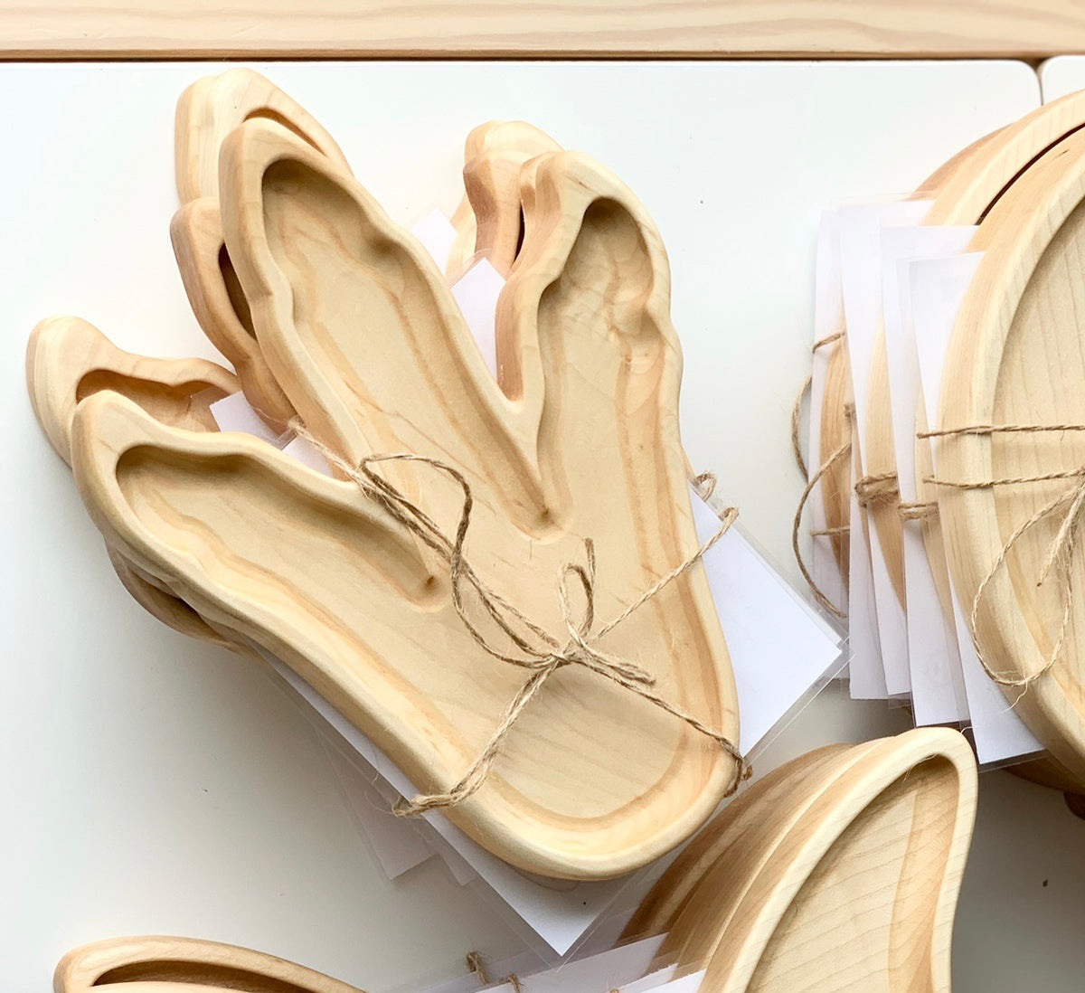 Natural wooden Dinosaur Footprint Plate shaped sensory trays stacked and tied with twine on white surface