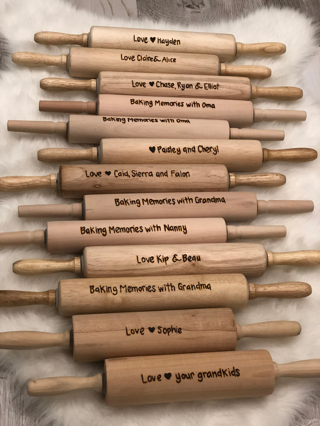 Collection of natural wood personalized rolling pins with custom burned messages and hearts displayed on a soft white surface