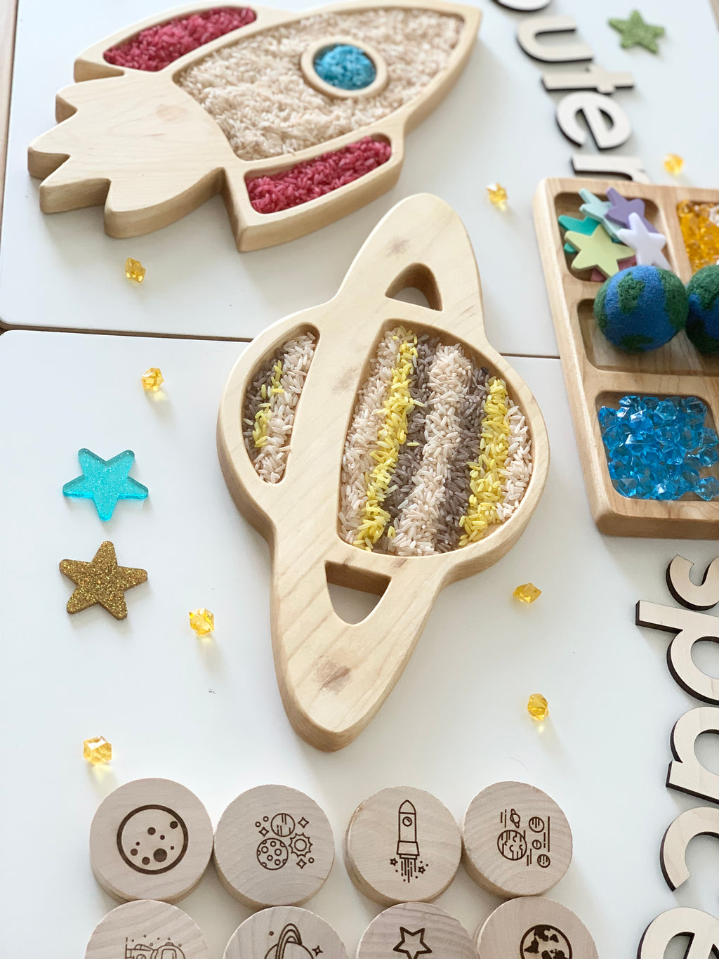 Natural wooden Saturn planet sensory tray filled with colored rice on white surface with star-shaped decorations