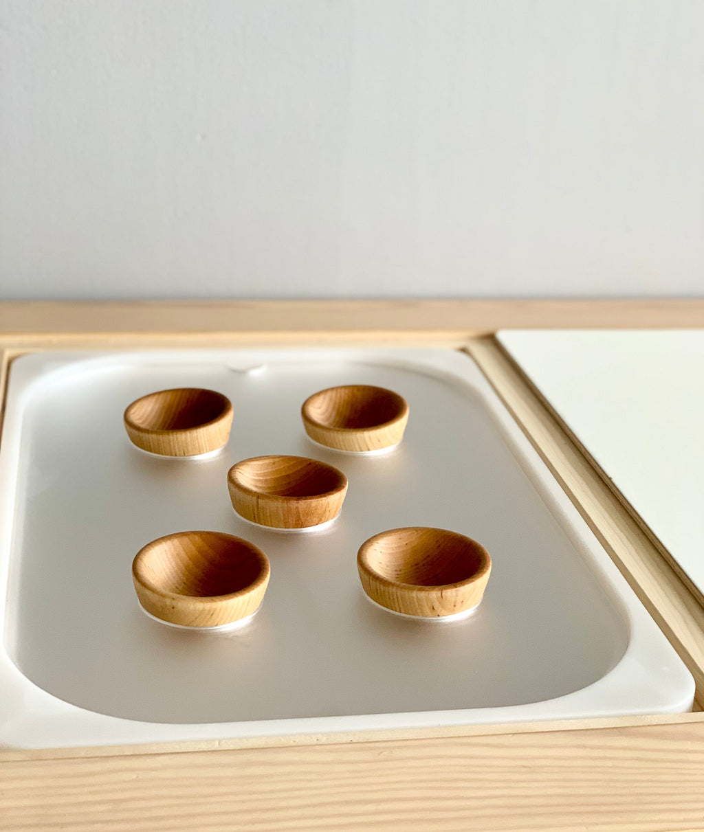Set of five small wooden bowls placed on a white acrylic insert in a light wood tray frame