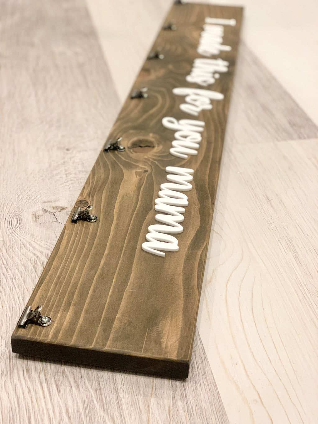 Long custom wooden sign stained brown with white cursive letters and metal clips for displaying children’s artwork