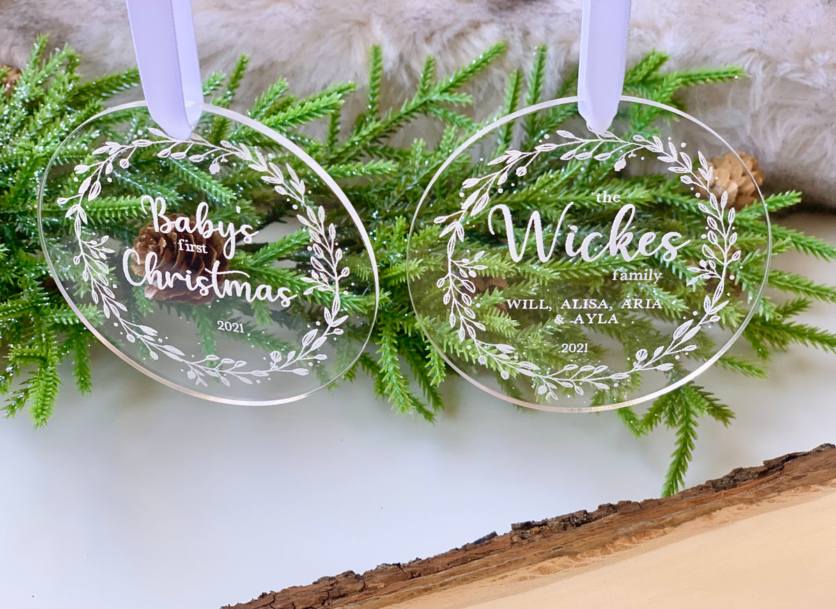 Two 3.5-inch round acrylic Christmas ornaments engraved with white family names and decorative wreath designs