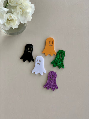 Set of five small laser-cut acrylic ghost shapes in black, orange, white, green glitter, and purple glitter on neutral surface