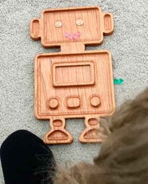 Wooden robot-shaped sensory tray with engraved facial features and buttons on light carpet background