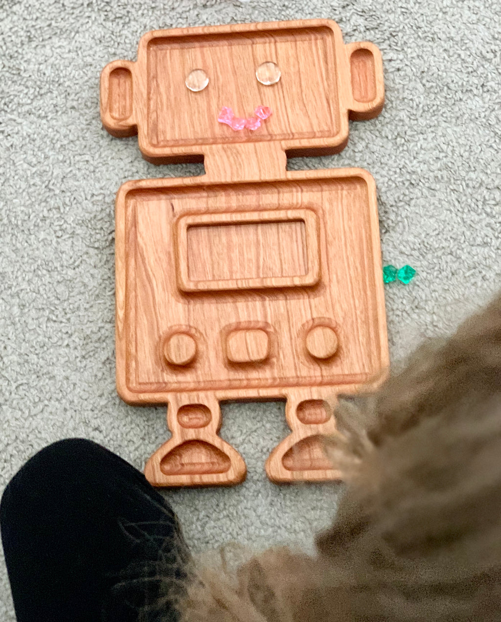 Wooden robot-shaped sensory tray with engraved facial features and buttons on light carpet background