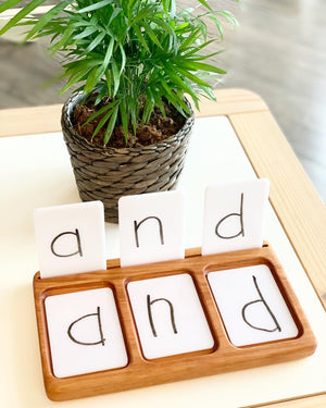 Wooden three-section sensory tray with dry erase flash cards spelling "and" on white background near green potted plant