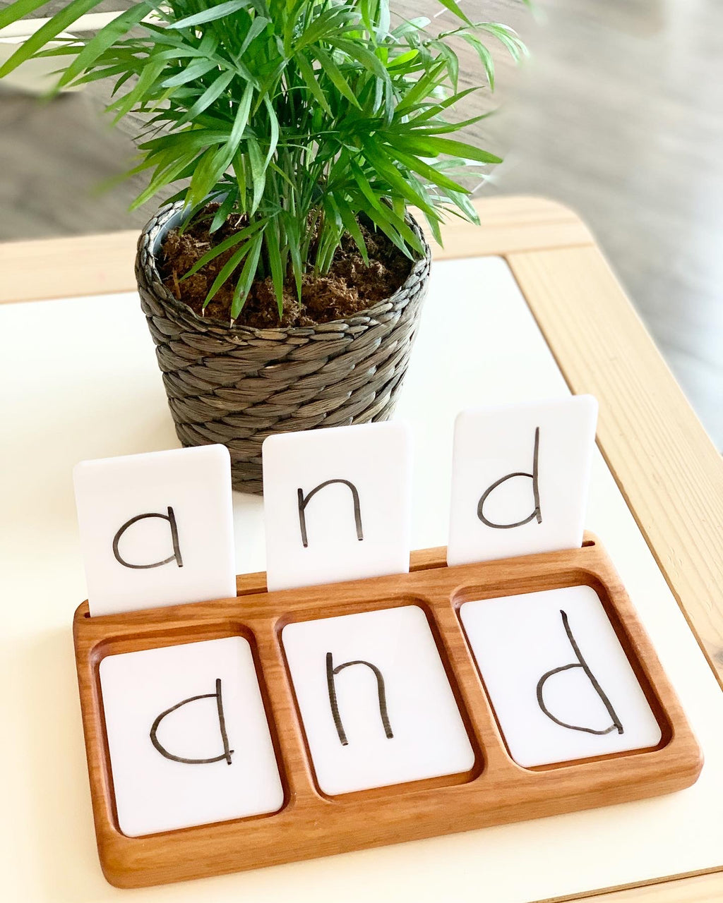Wooden three-section sensory tray with dry erase flash cards spelling "and" on white background near green potted plant