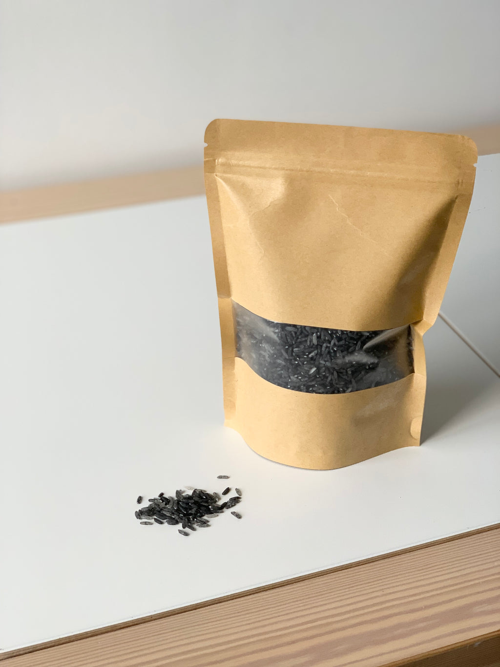 Brown stand-up pouch with black rice sensory filler spilling on white surface with light wood trim background