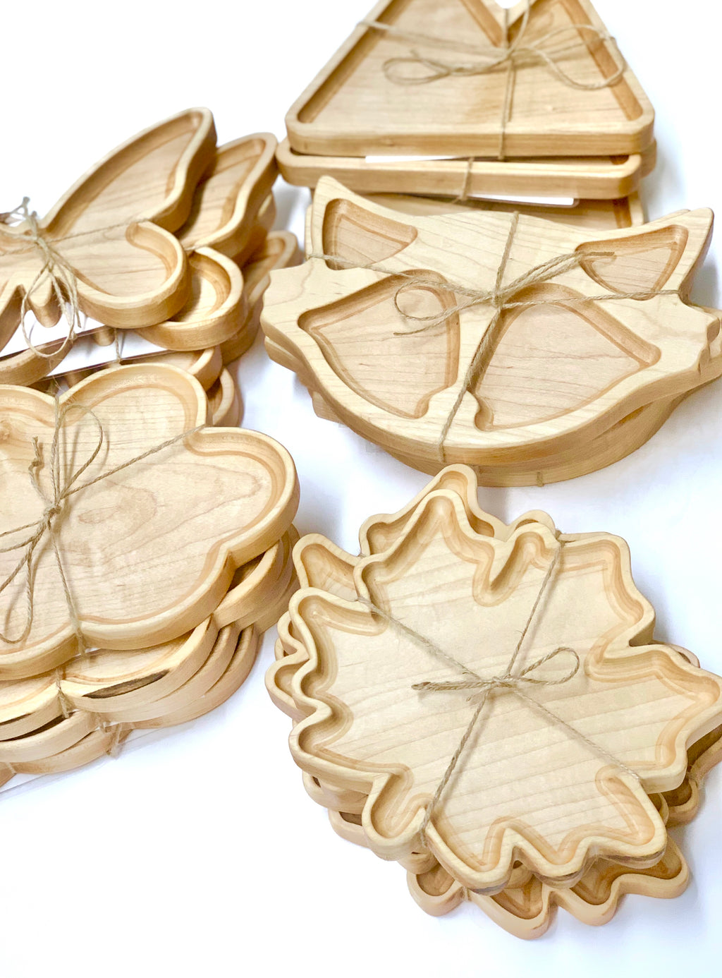 Stacks of natural wooden sensory trays shaped like fox, butterfly, leaf, and triangle tied with twine on white background