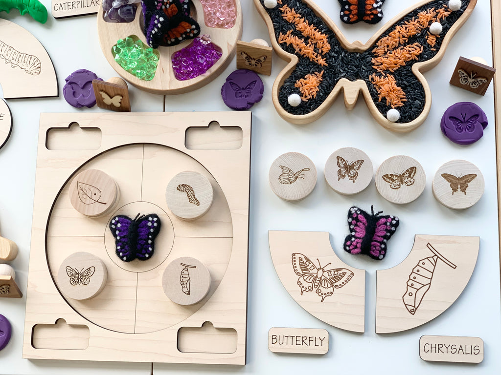 Natural wooden butterfly sensory tray with engraved insect stages and colorful butterfly figures on white surface