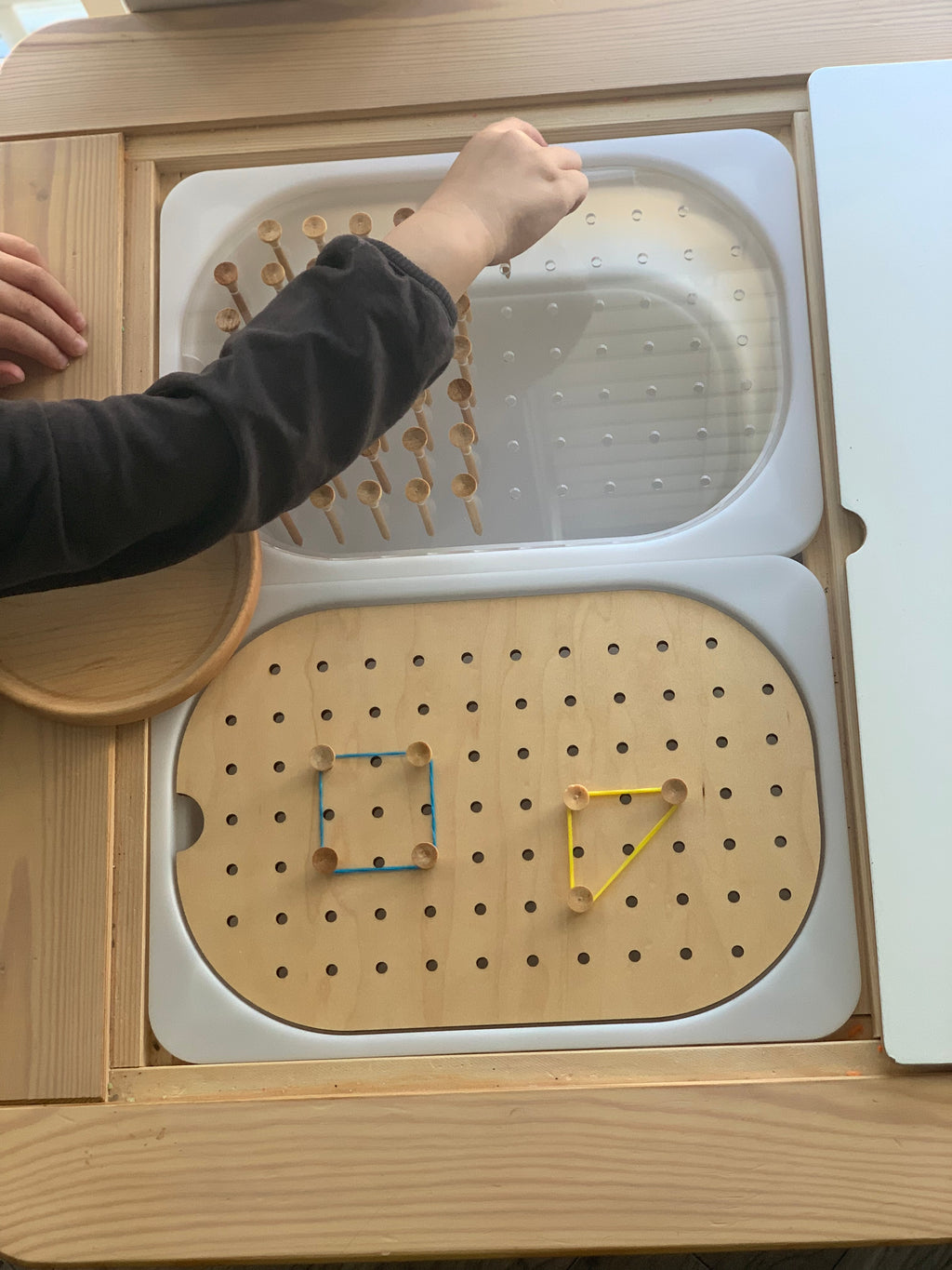 Child’s hand placing golf tee pegs into a Flisat peg board with wooden elastic band shapes on table insert