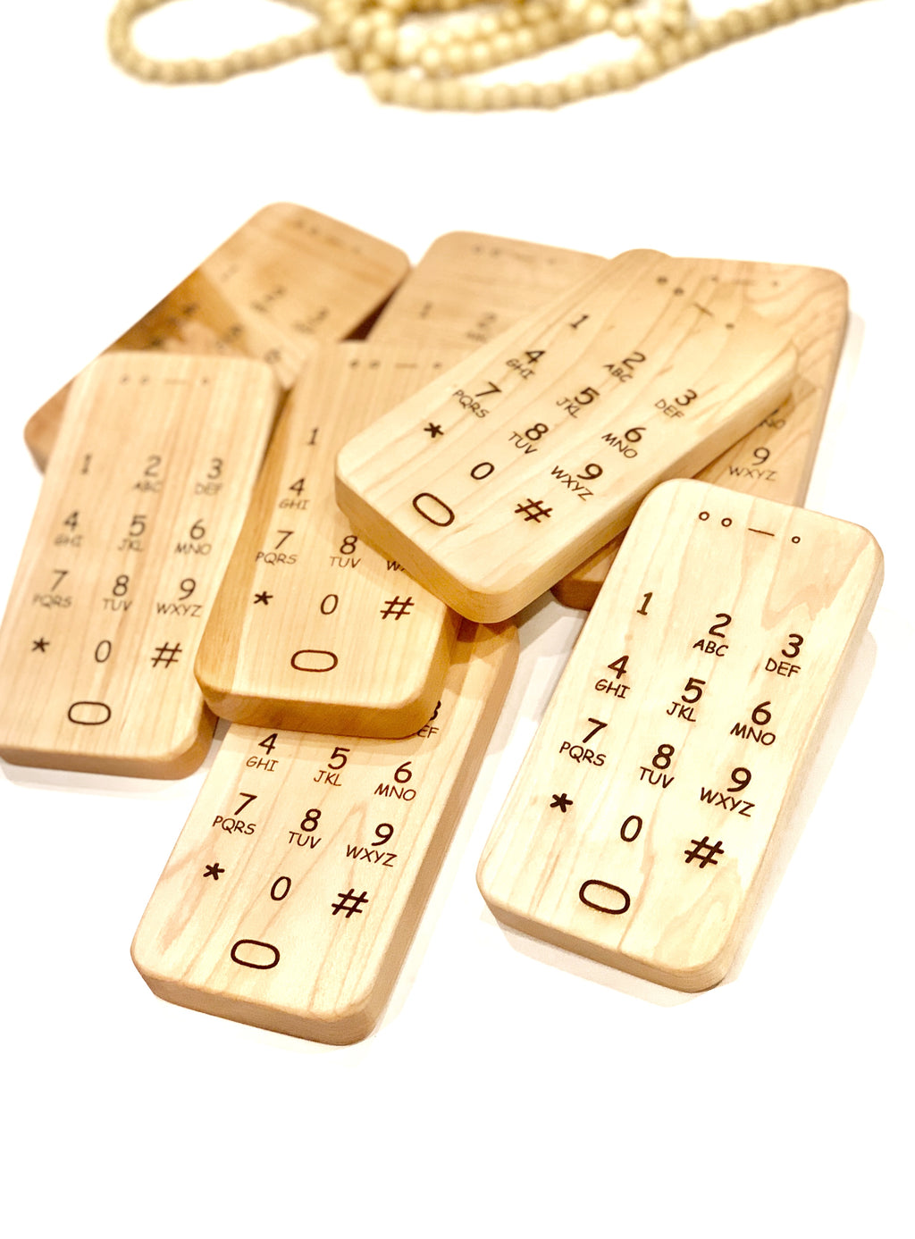 Multiple natural wooden toy phones with engraved numbers and symbols stacked on white background