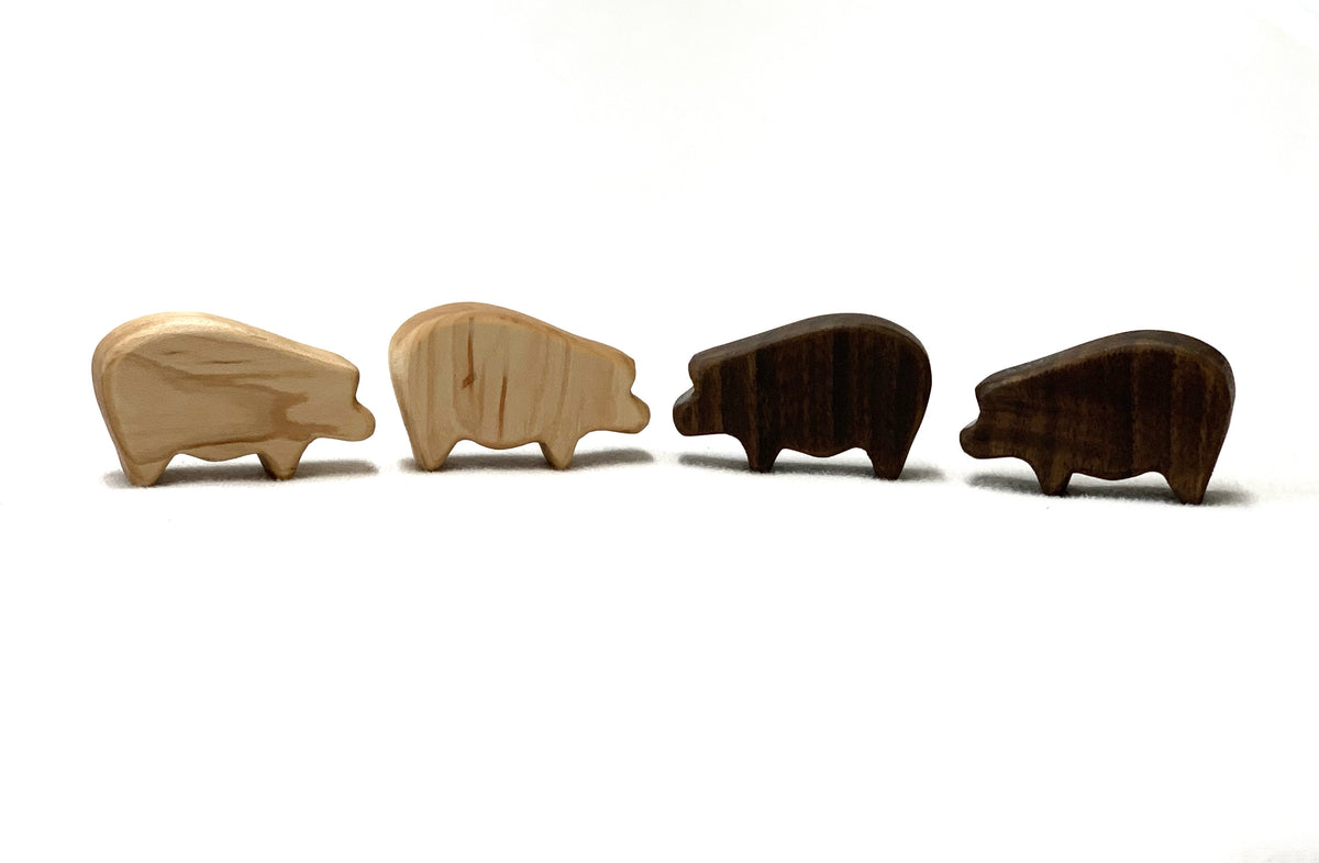 Four small wooden farm animal toy figurines in light and dark wood finishes on white background