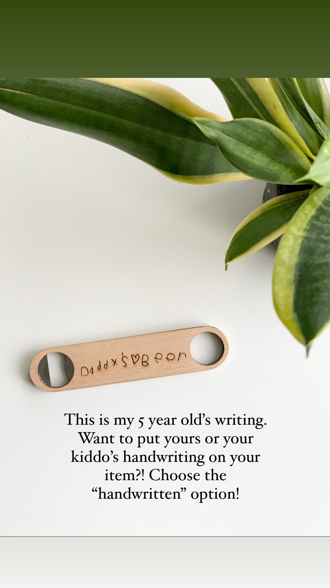 Custom wooden bottle opener engraved with child’s handwriting spelling "Daddy’s Beer" on white background with green plant