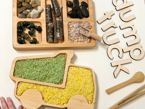 Wooden dump truck shaped sensory tray filled with colored rice, natural stones, and wooden scoop on white surface