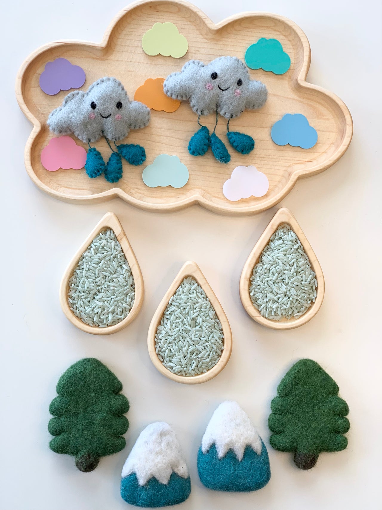 Natural wooden cloud-shaped tray with colorful paper clouds, felt rain clouds, raindrop plates filled with rice, and felt trees and mountains