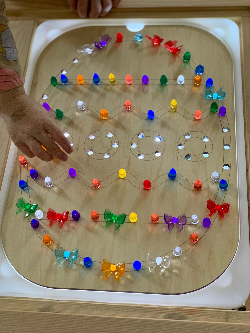 Light-up colorful LED string arranged on wooden geometric board with child's hand reaching over white light table