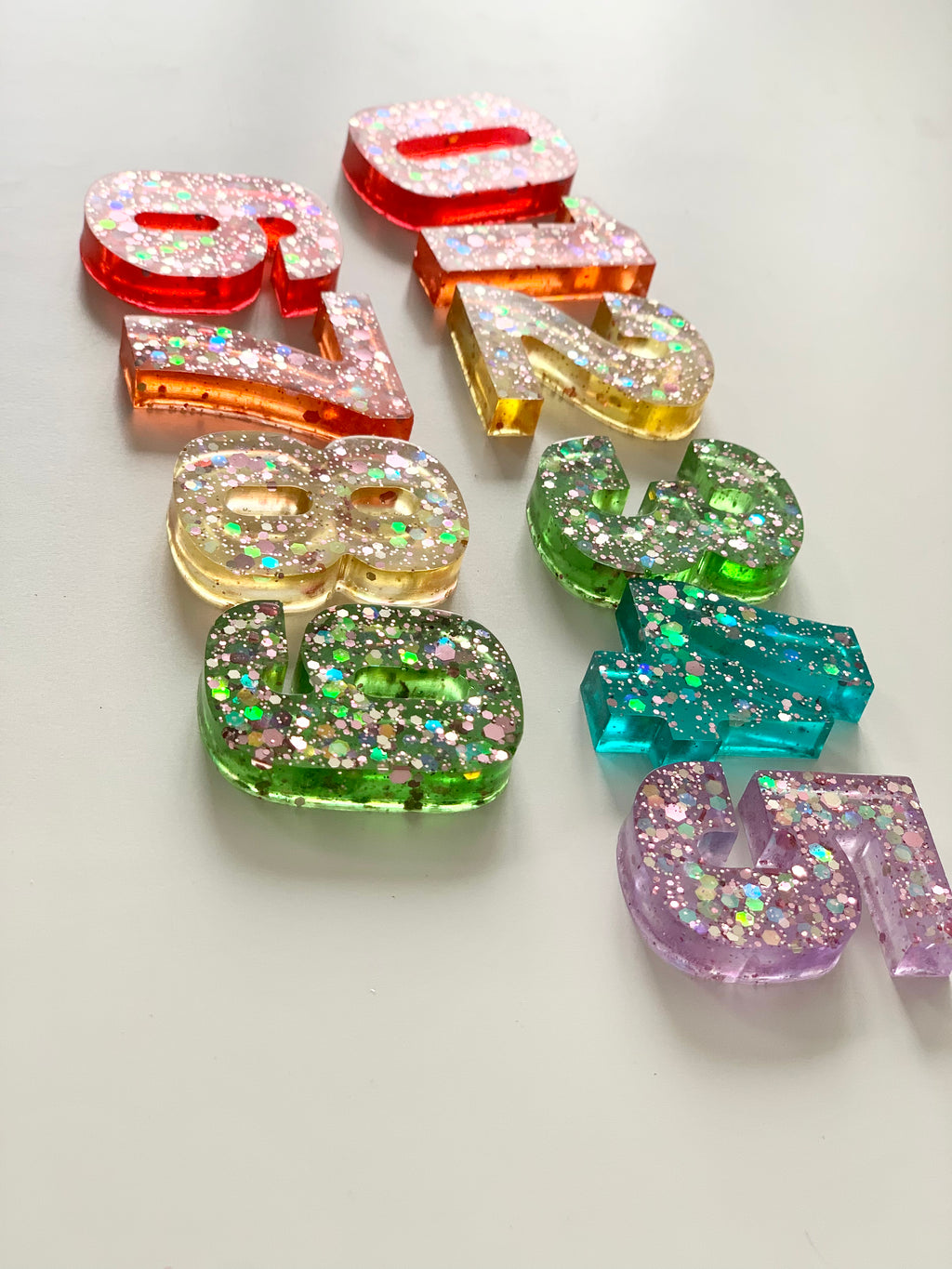 Rainbow glitter resin numbers in various colors arranged on white surface, designed to fit Flisat insert tray