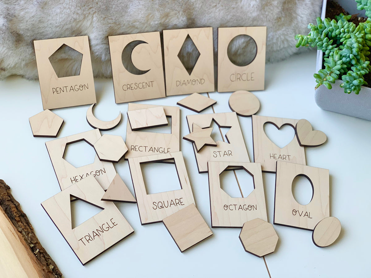 Natural wooden shape puzzle flash cards with cutouts and matching pieces labeled with shape names on white surface near plant