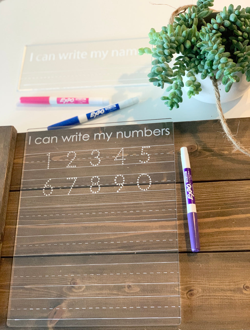 Clear acrylic dry erase board engraved with "I can write my numbers" and dotted numbers for tracing with markers nearby