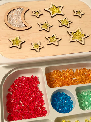 Wooden night sky tabletop insert with moon and stars filled with clear and yellow gems above a tray of colorful translucent beads
