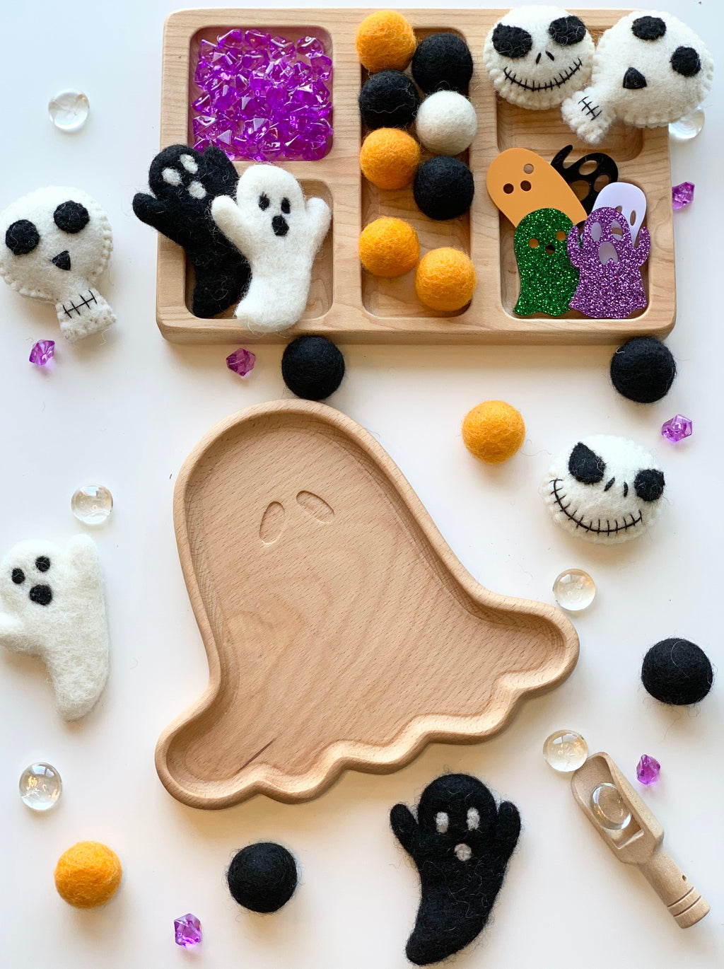 Natural wooden ghost-shaped sensory tray surrounded by felt ghost and skull toys with colorful craft materials on white background